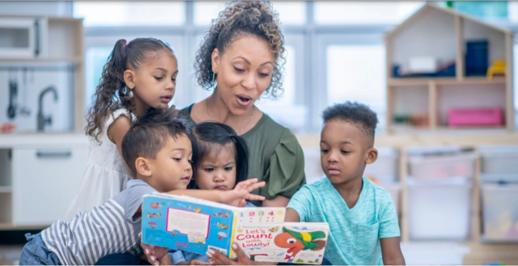 Teacher reading a picture book to young children in a bright classroom.