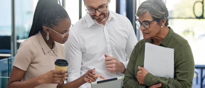 Diverse business professionals collaborate on a tablet in a bright office.
