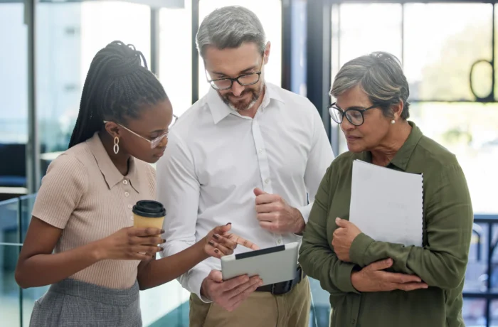 Diverse business professionals collaborate on a tablet in a bright office.