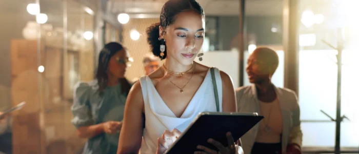 A focused woman uses a tablet in a busy, brightly lit office.