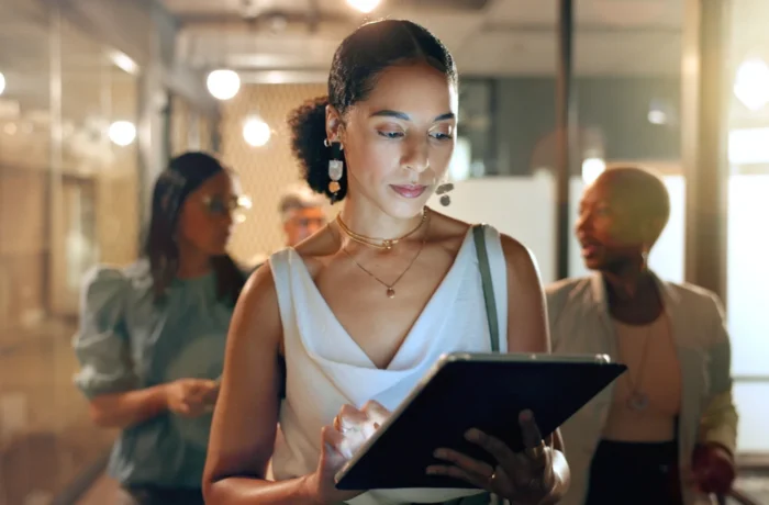 A focused woman uses a tablet in a busy, brightly lit office.